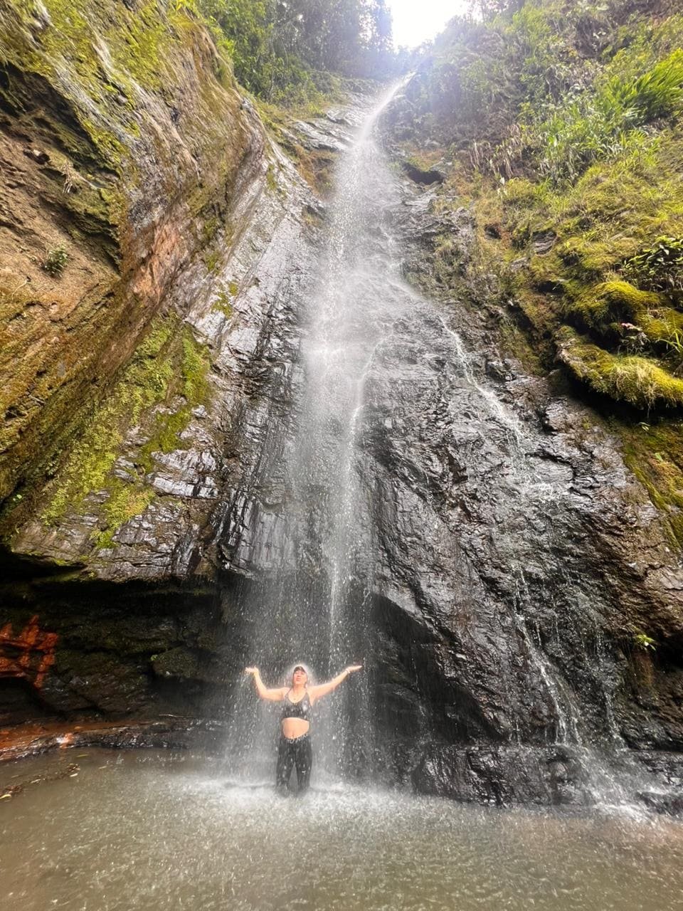 foto de una persona debajo de la caida de la cascada chupal
